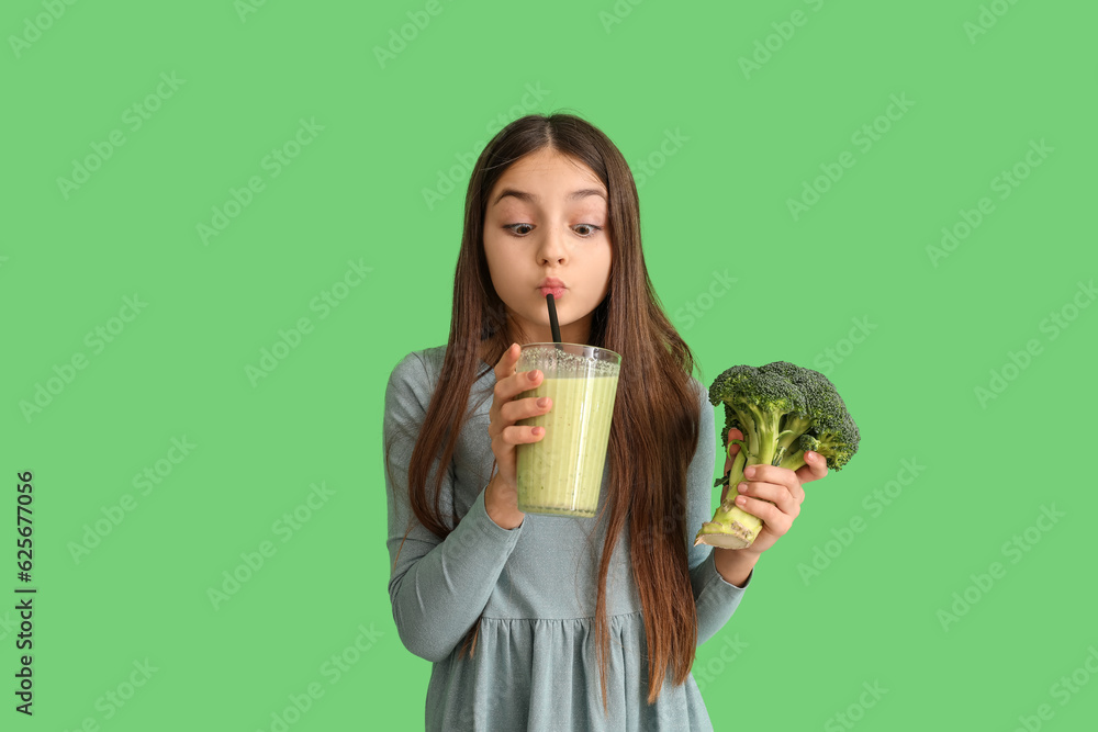 Little girl with broccoli drinking smoothie on green background