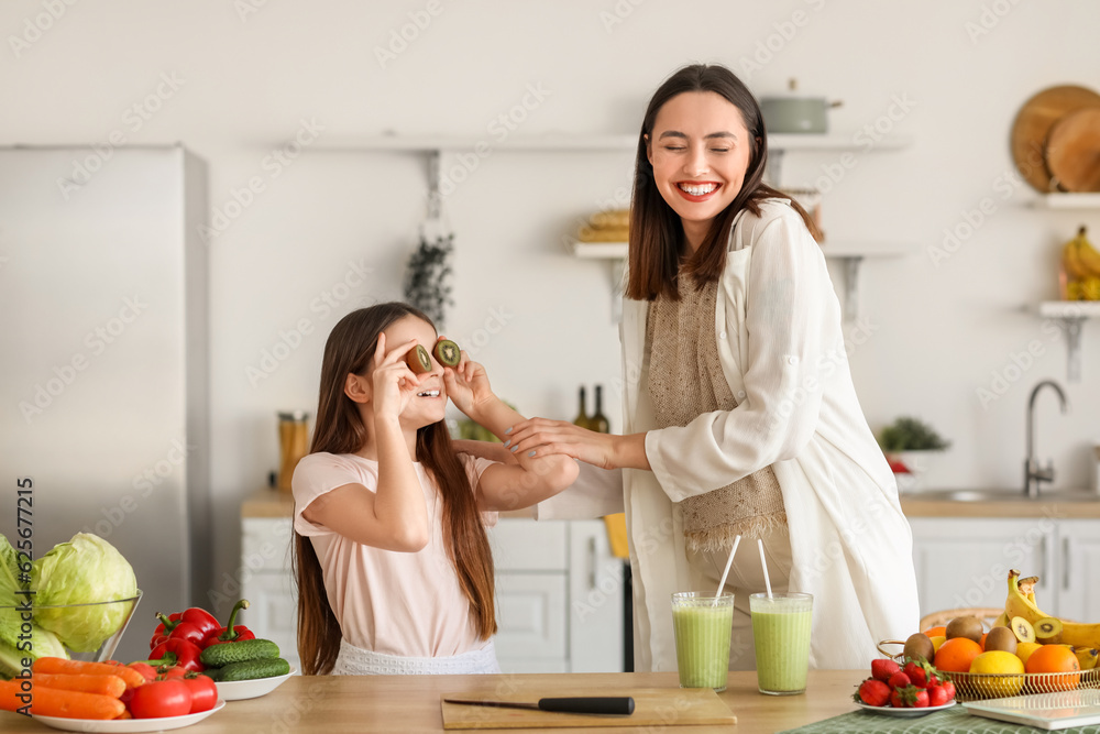 Little girl with her pregnant mother drinking green smoothie in kitchen