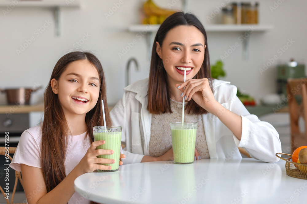 Little girl with her mother drinking green smoothie at table in kitchen