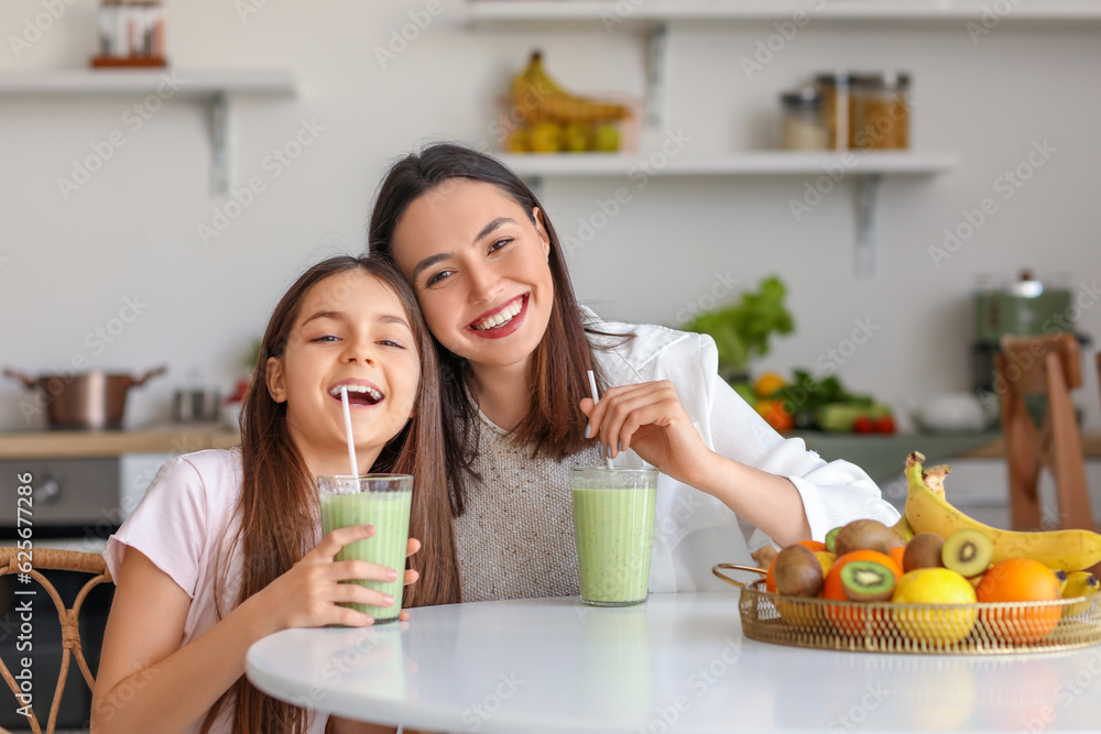 Little girl with her mother drinking green smoothie at table in kitchen