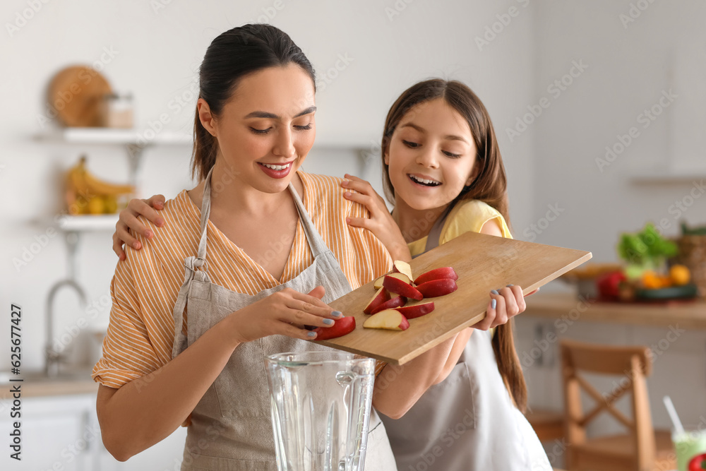 Little girl with her mother putting cut apple into blender in kitchen