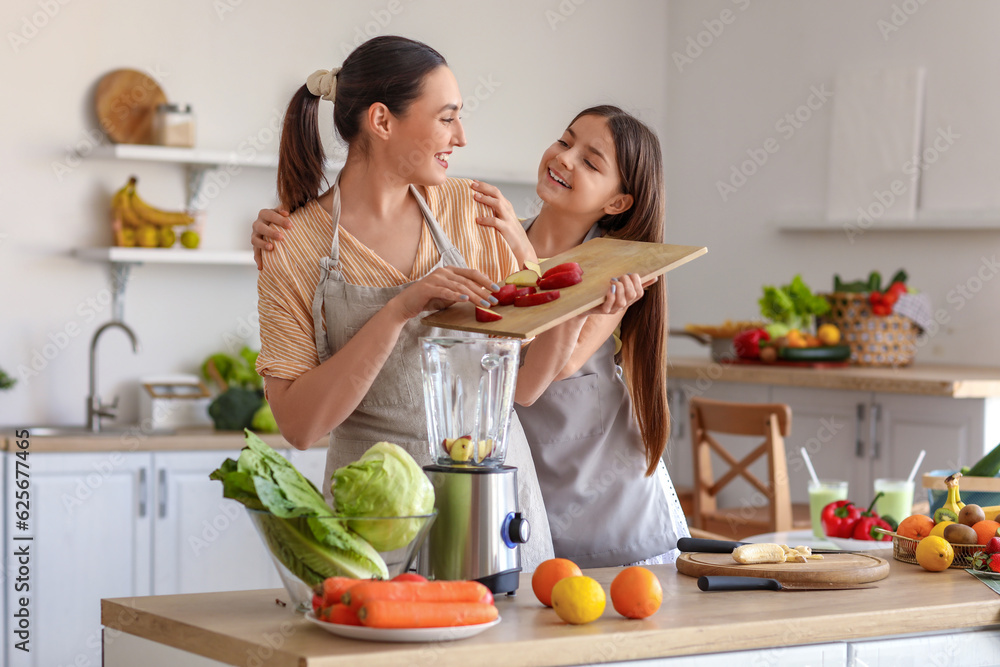 Little girl with her mother putting cut apple into blender in kitchen