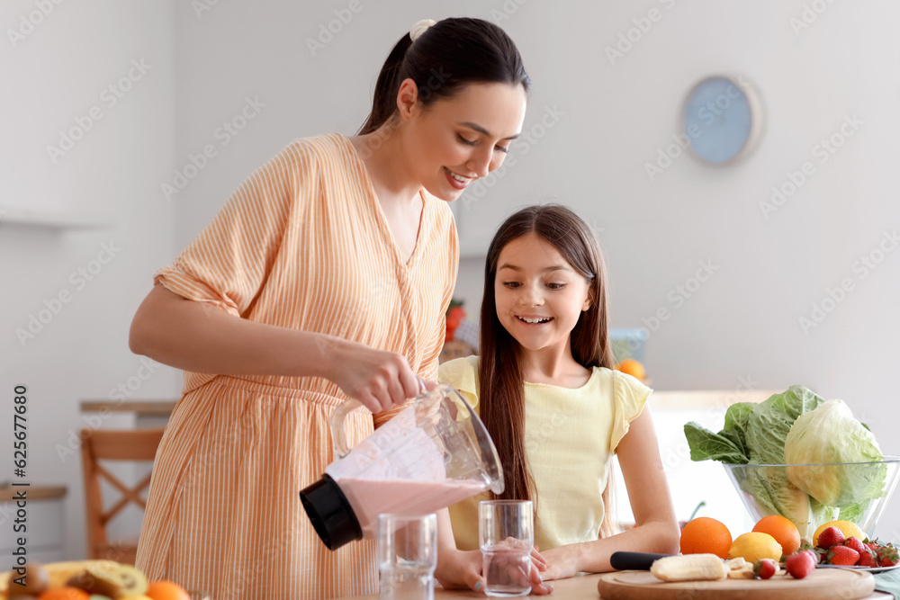 Young woman with her little daughter pouring fresh smoothie into glass in kitchen