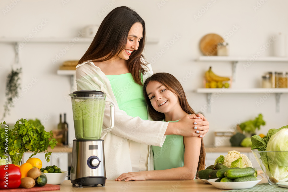 Little girl and her mother making vegetable smoothie with blender in kitchen