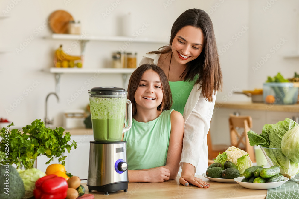 Little girl and her mother making vegetable smoothie with blender in kitchen