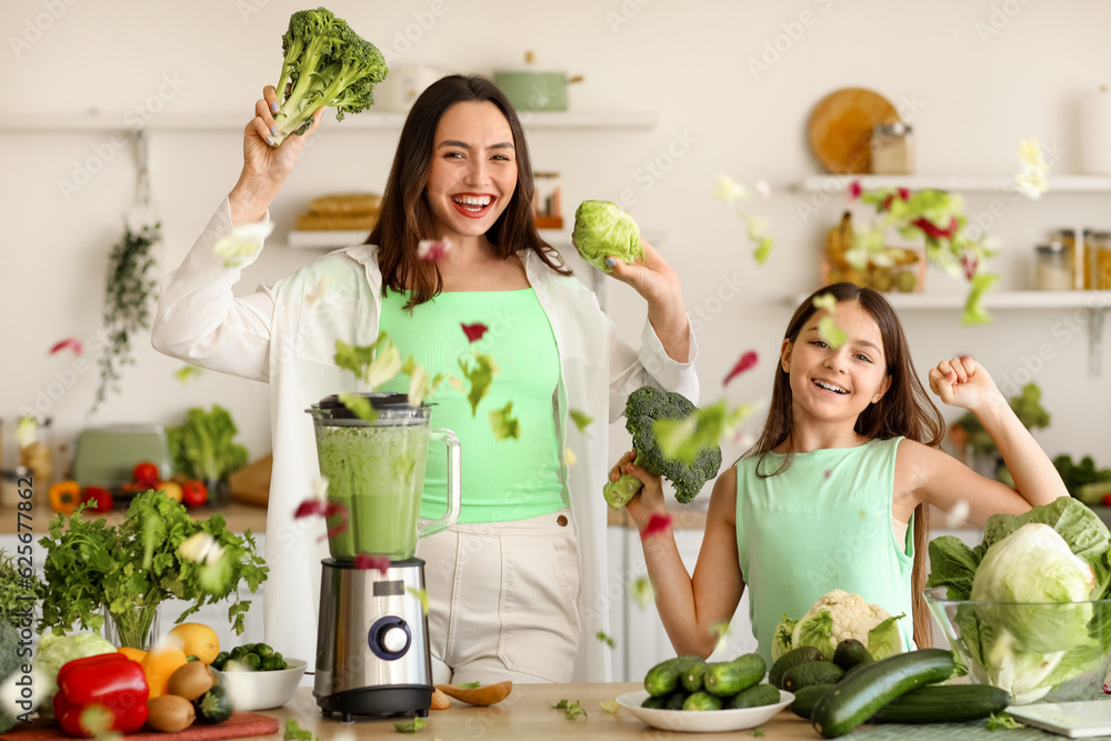 Little girl and her mother making vegetable smoothie with blender in kitchen