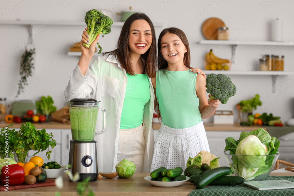 Little girl and her mother making vegetable smoothie with blender in kitchen