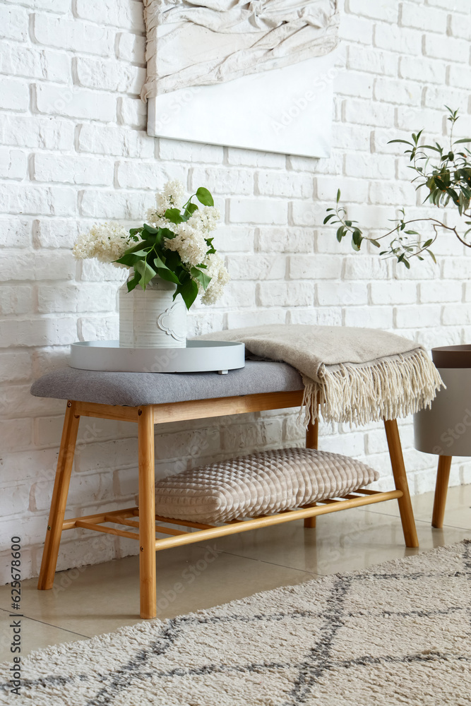 Vase with lilac flowers on soft bench in room