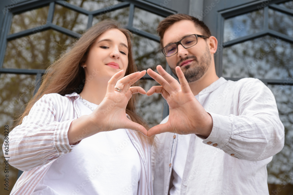 Beautiful happy couple making heart shape with their hands in city