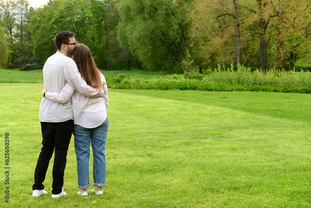 Young man kissing his girlfriend on her head in beautiful park