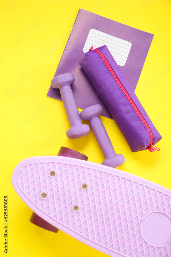 Skateboard with dumbbells, pencil case and notebook on yellow background