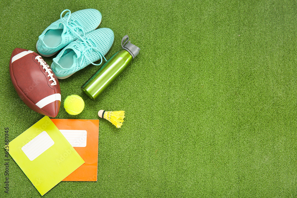 Sneakers with sport balls, bottle of water and notebooks on color background