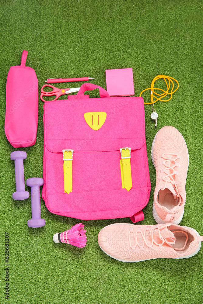 Backpack with sport equipment and different stationery on color background