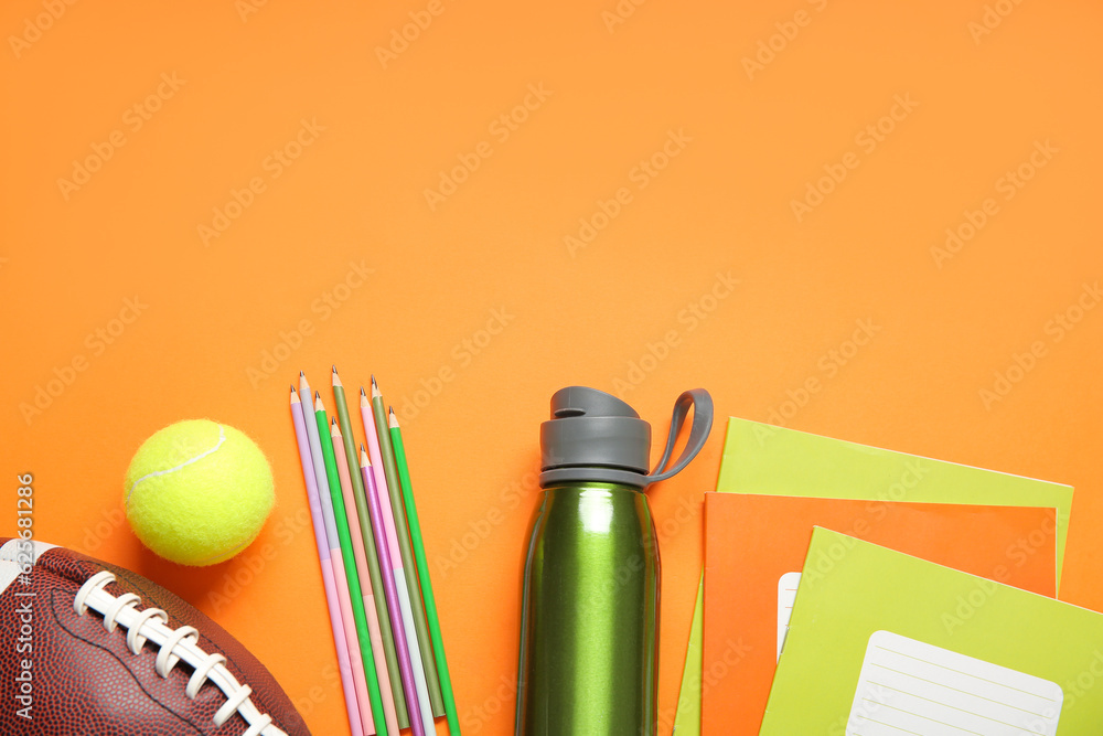 Bottle of water with different stationery, rugby and tennis balls on orange background