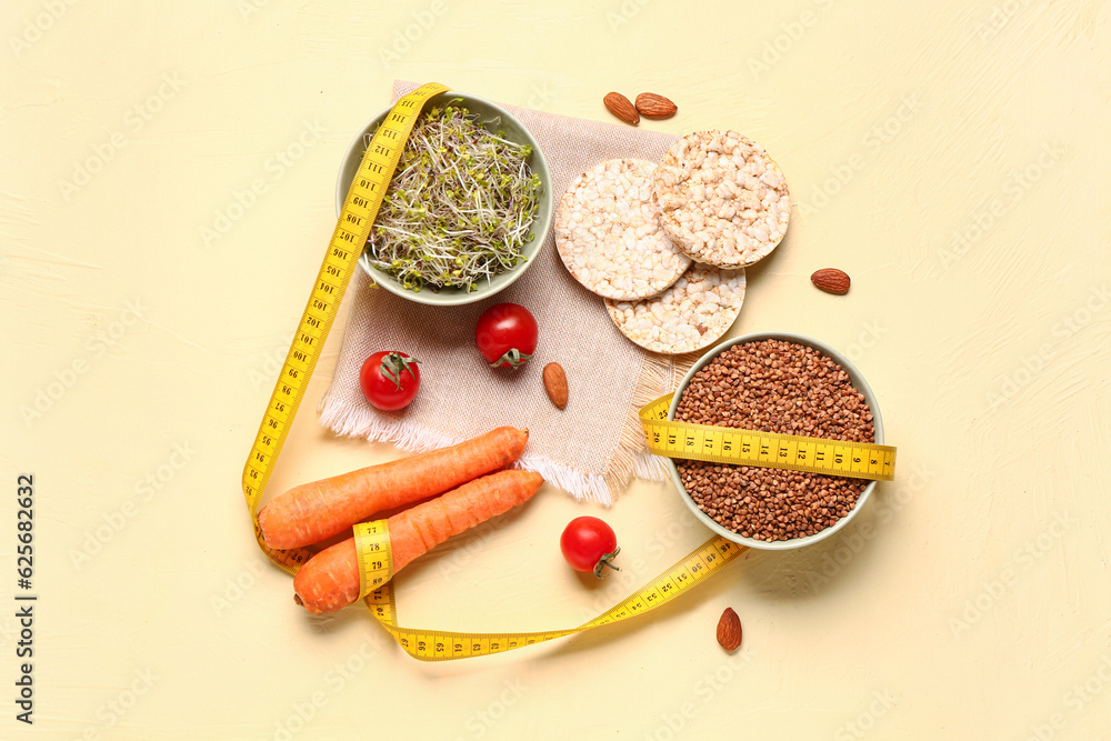 Bowls of microgreens, buckwheat with vegetables and measuring tape on yellow background. Diet concep