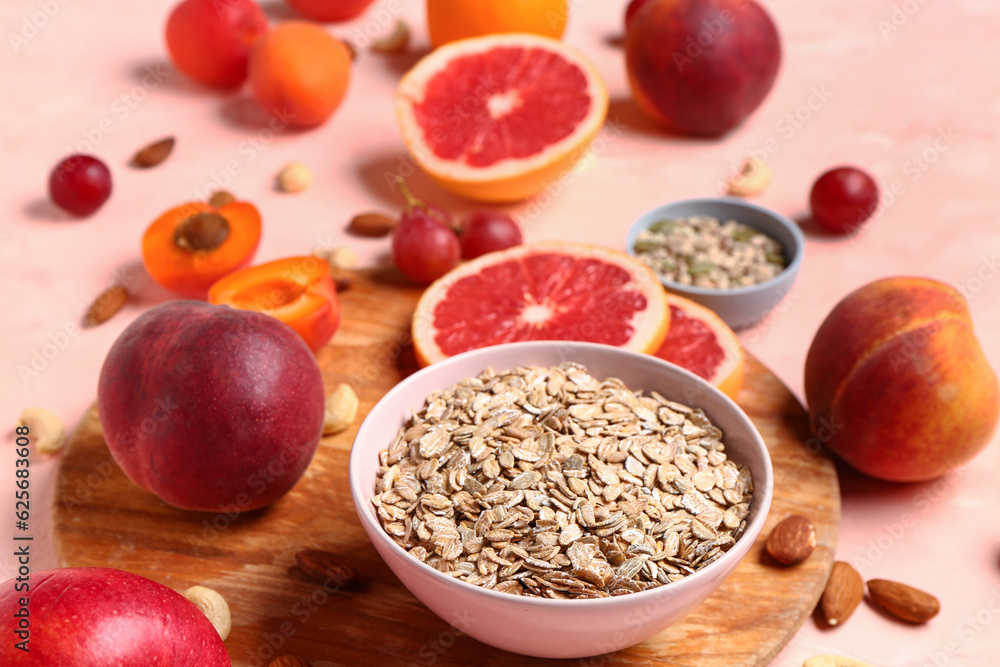 Bowl with oatmeal and fresh fruits on pink background