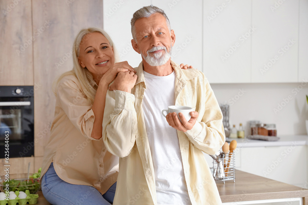 Mature man with cup of coffee and his wife in kitchen