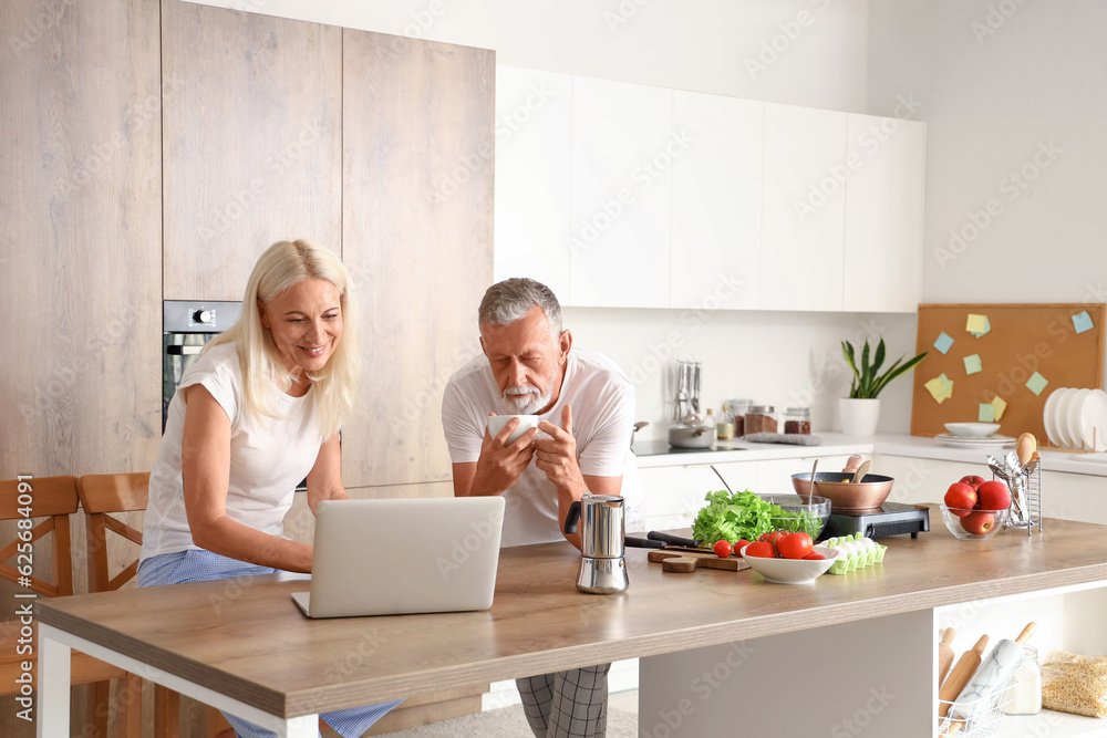 Mature couple with laptop drinking coffee in kitchen