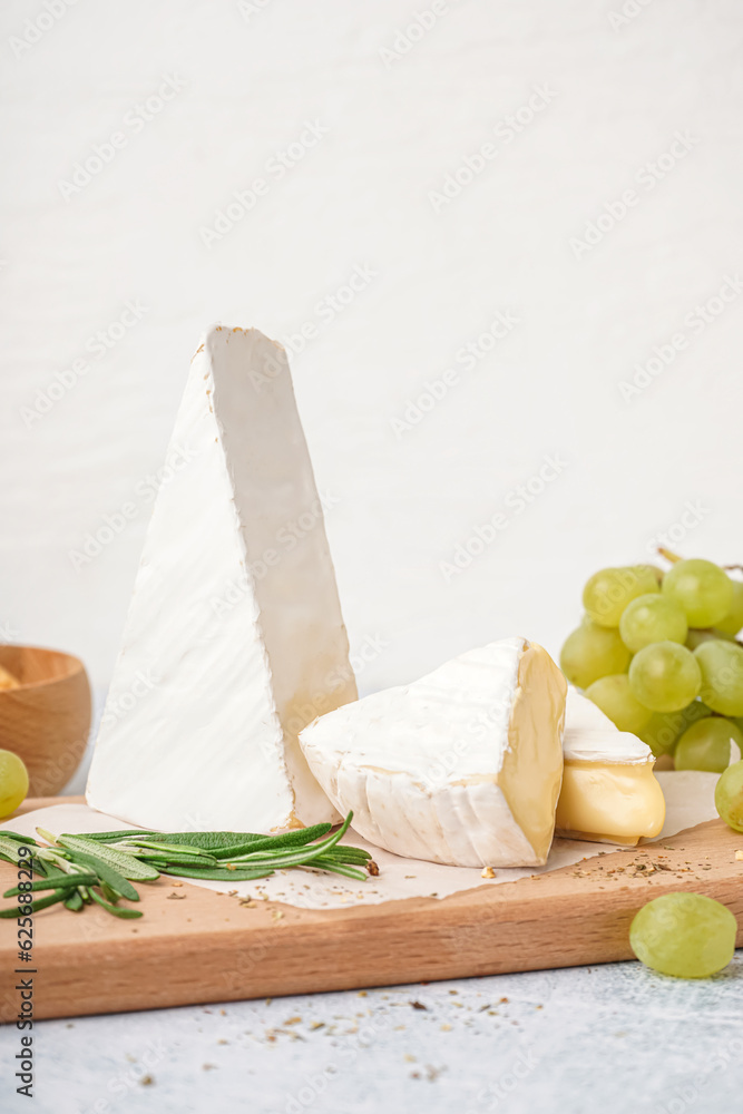 Wooden board with tasty Camembert cheese on light background