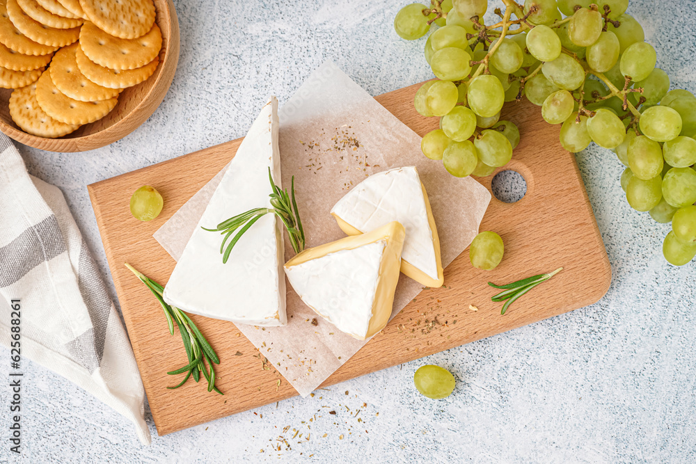 Wooden board with tasty Camembert cheese on light background