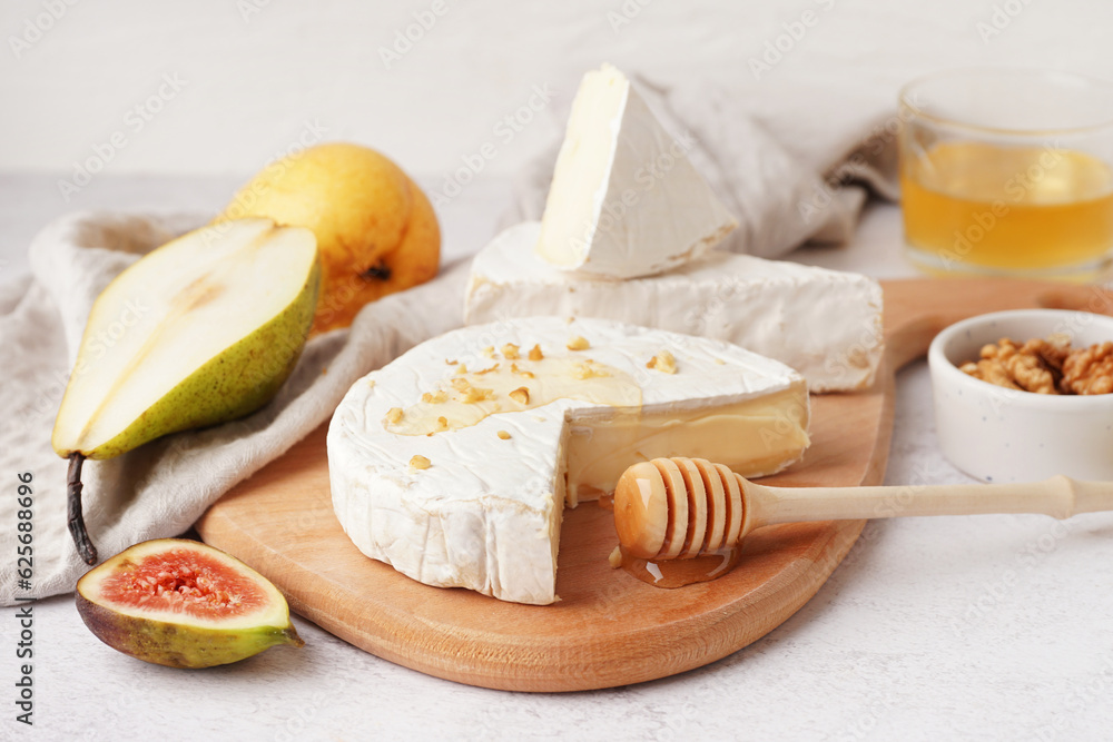 Wooden board with pieces of tasty Camembert cheese on light background