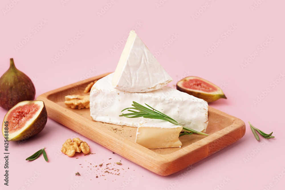 Wooden board with pieces of tasty Camembert cheese on pink background