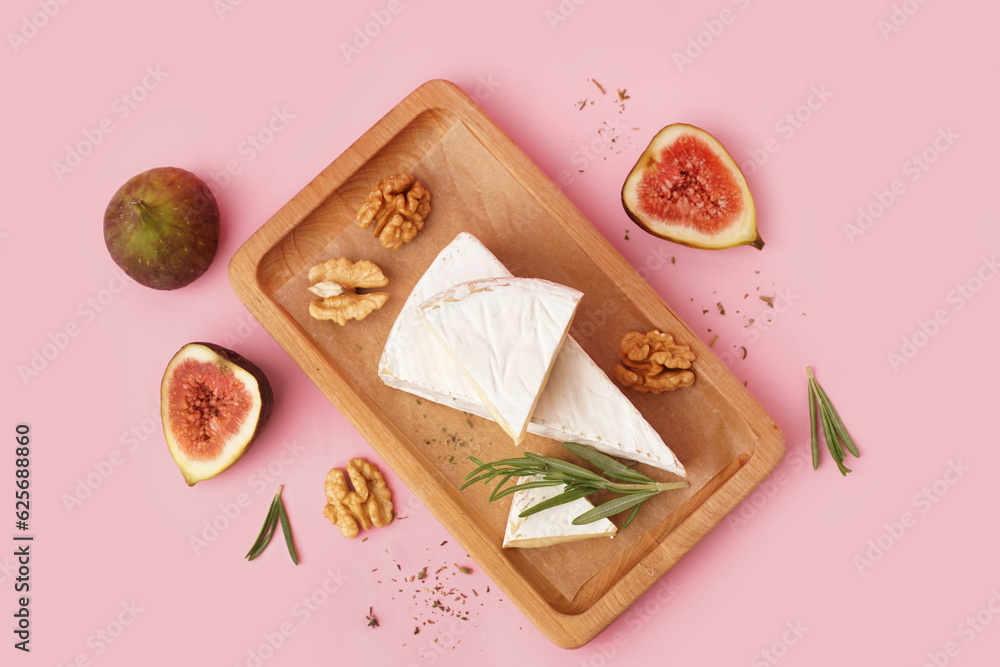 Wooden board with pieces of tasty Camembert cheese on pink background