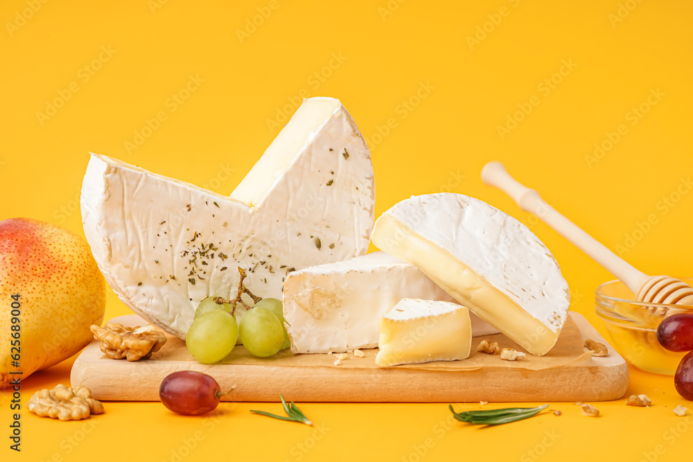 Wooden board with pieces of tasty Camembert cheese on yellow background