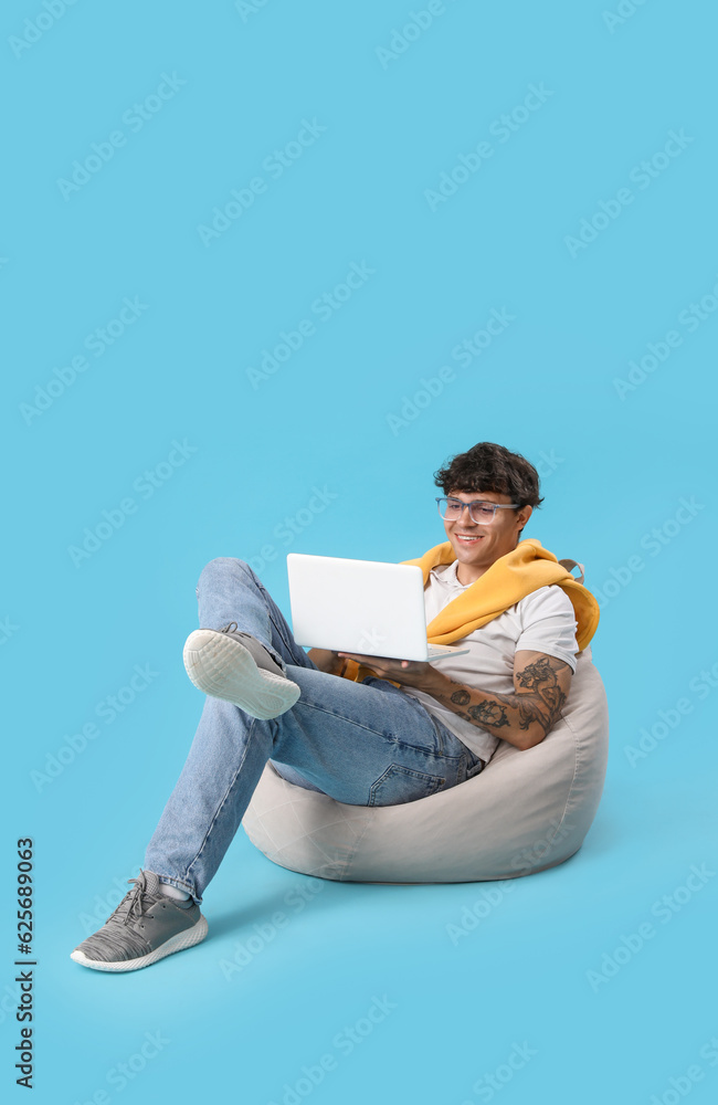 Young man using laptop in beanbag on blue background