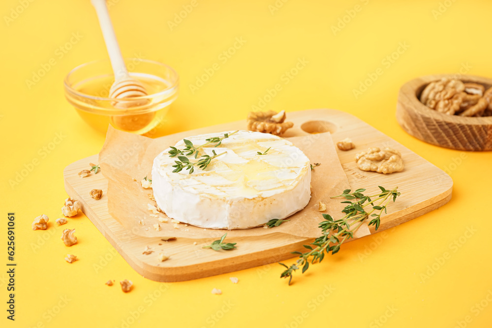 Wooden board of tasty baked Camembert cheese on yellow background