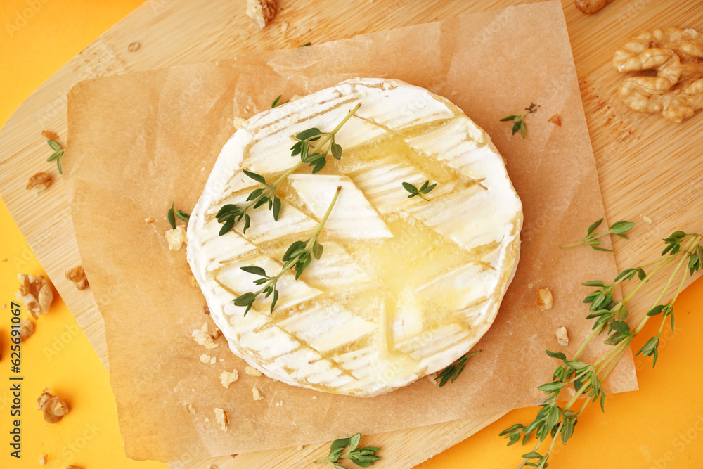 Wooden board of tasty baked Camembert cheese on yellow background