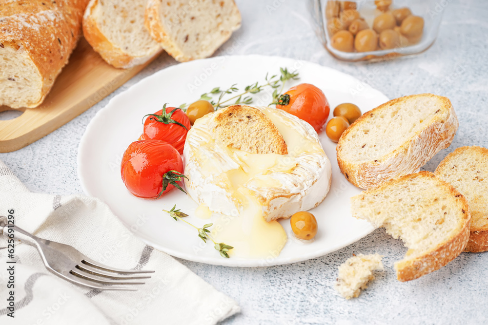 Plate of tasty baked Camembert cheese on light background