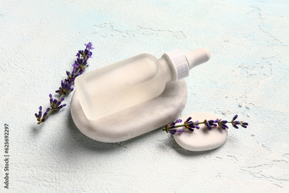 Composition with bottle of essential oil, spa stones and lavender flowers on light background