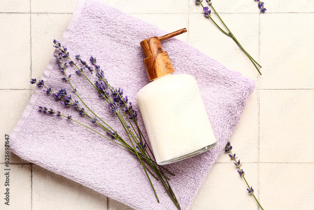 Bottle of cosmetic product, clean towel and lavender flowers on light tile background