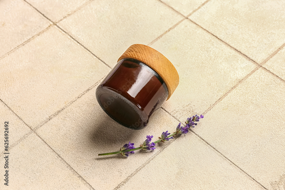 Jar of cosmetic product and lavender flower on light tile background