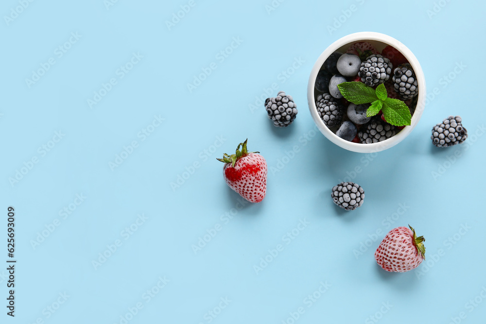 Bowl of frozen berries with mint leaves on blue background