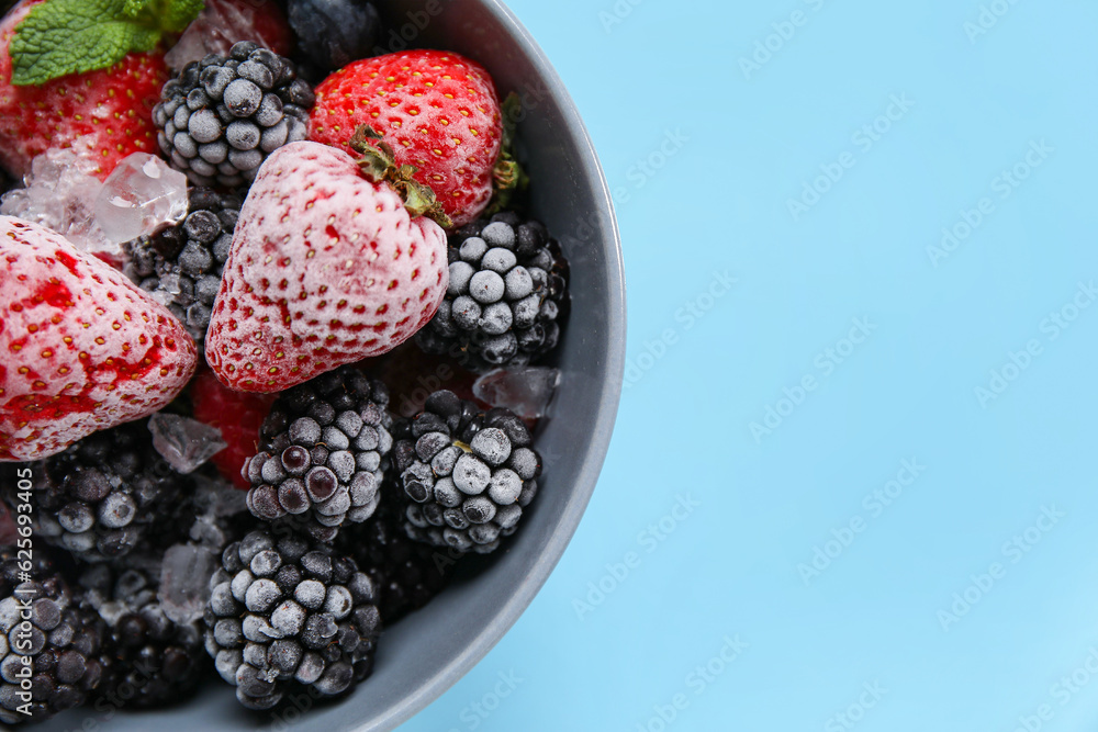 Bowl of frozen berries with mint leaves on blue background