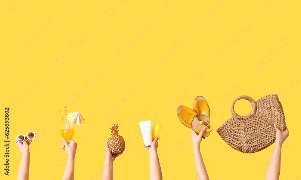 Many hands holding different beach accessories and cocktail on yellow background