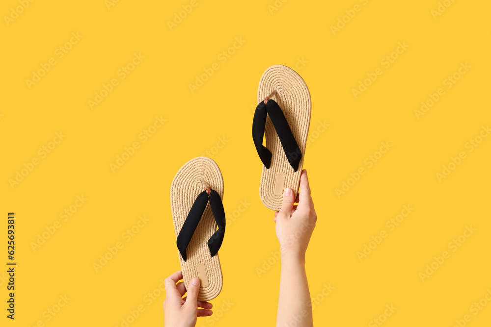 Female hands with flip flops on yellow background