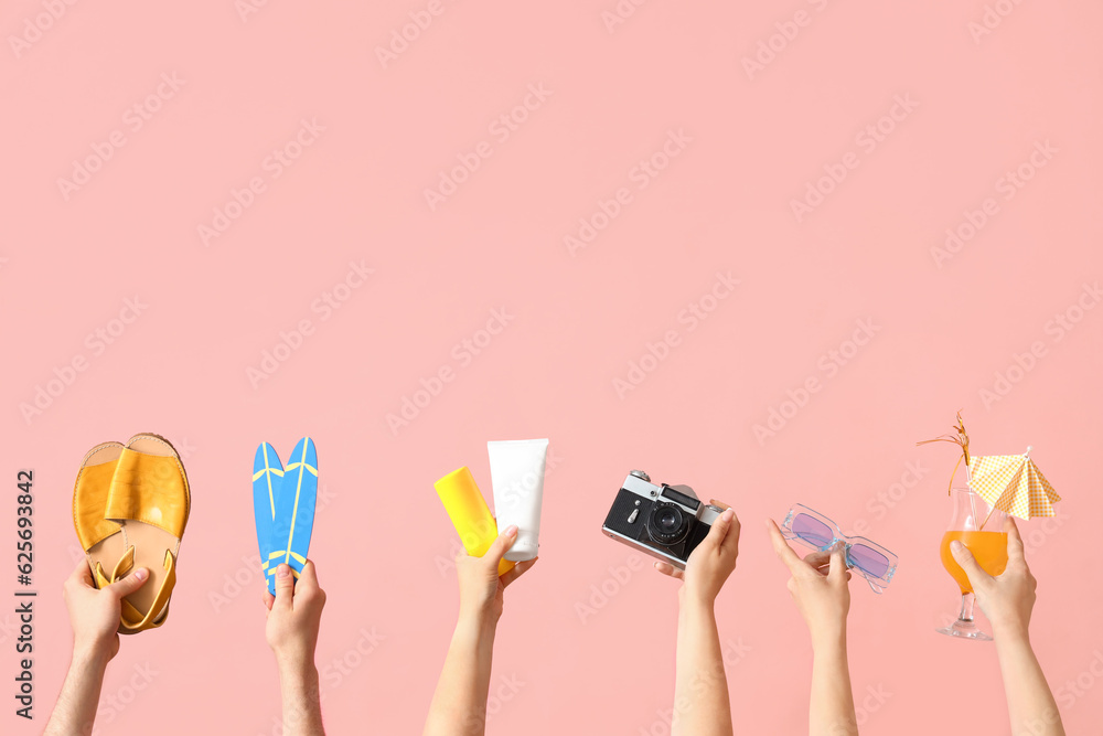 Many hands with beach accessories, cocktail and camera on pink background