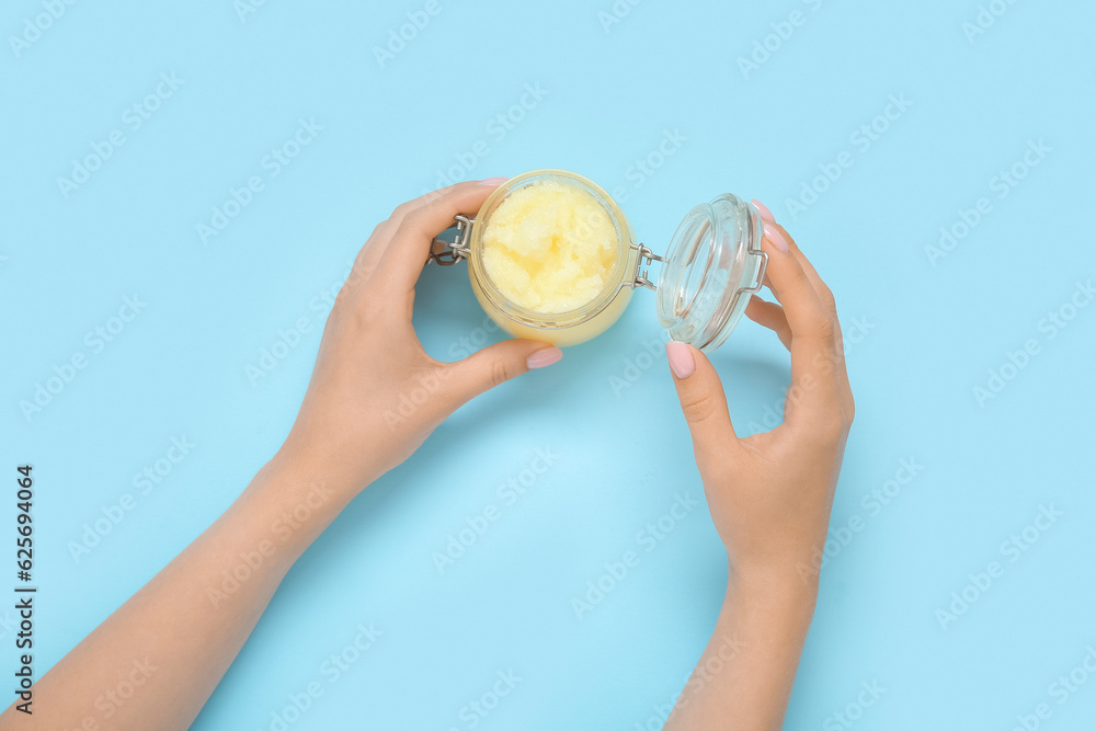 Female hands with jar of lemon body scrub on blue background