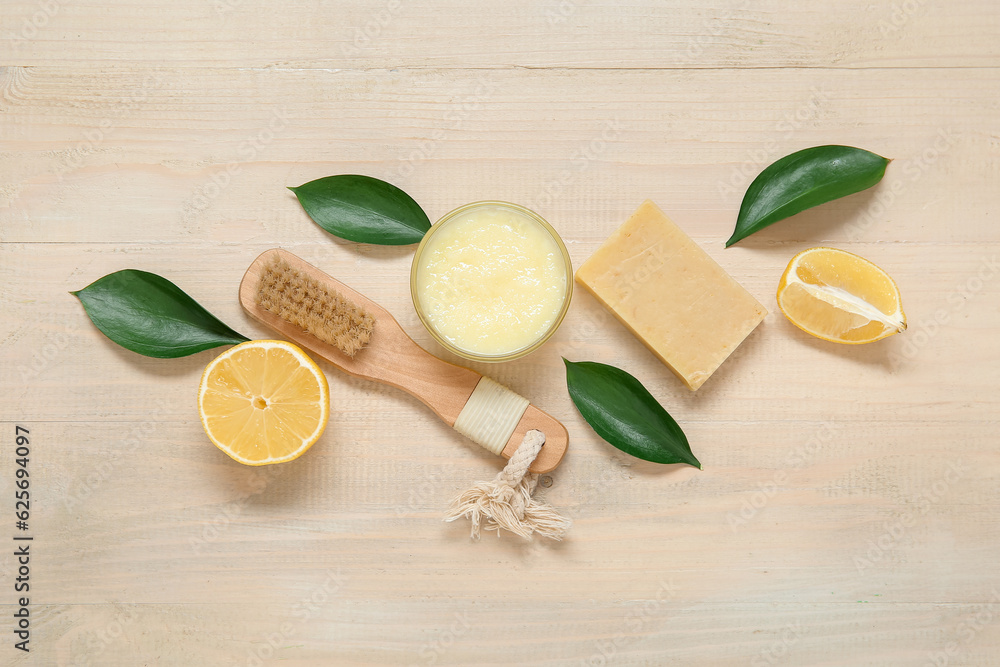 Bowl of lemon body scrub with massage brush and soap on beige wooden background