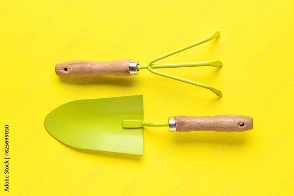 Gardening rake and shovel on yellow background