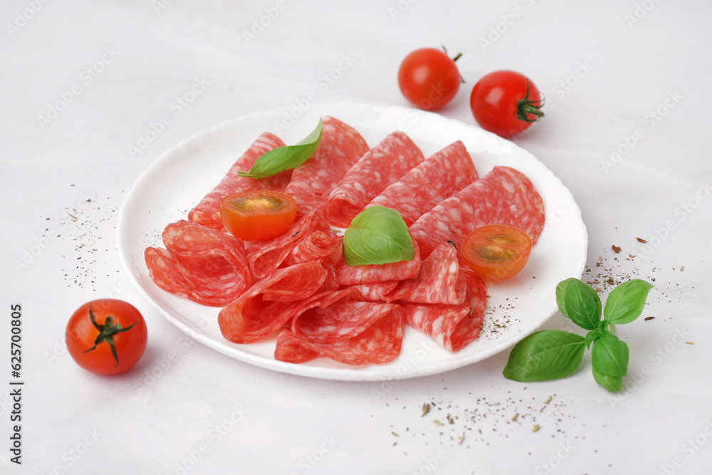 Plate with slices of tasty salami on light background