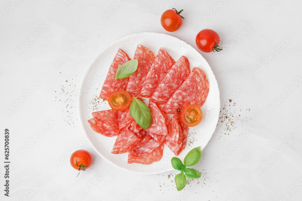 Plate with slices of tasty salami on light background