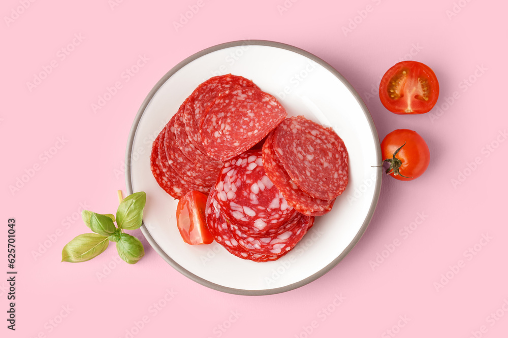 Plate with slices of tasty salami on pink background