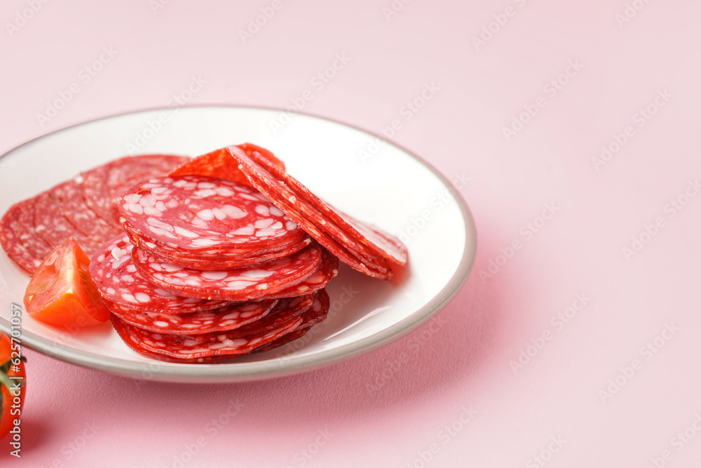 Plate with slices of tasty salami on pink background