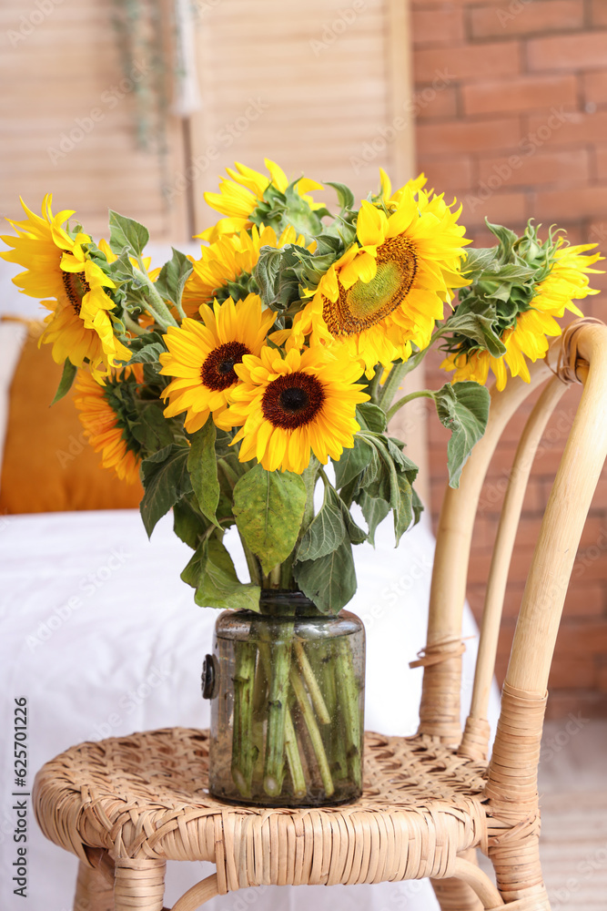 Vase with beautiful sunflowers on wicker chair in interior of stylish bedroom, closeup