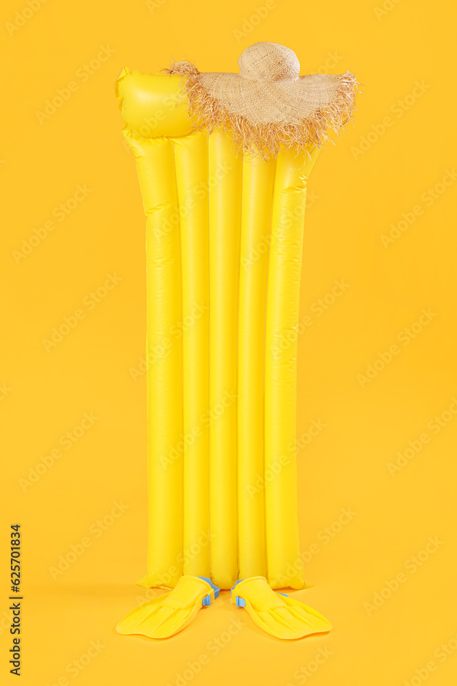 Inflatable mattress with flippers and hat on yellow background