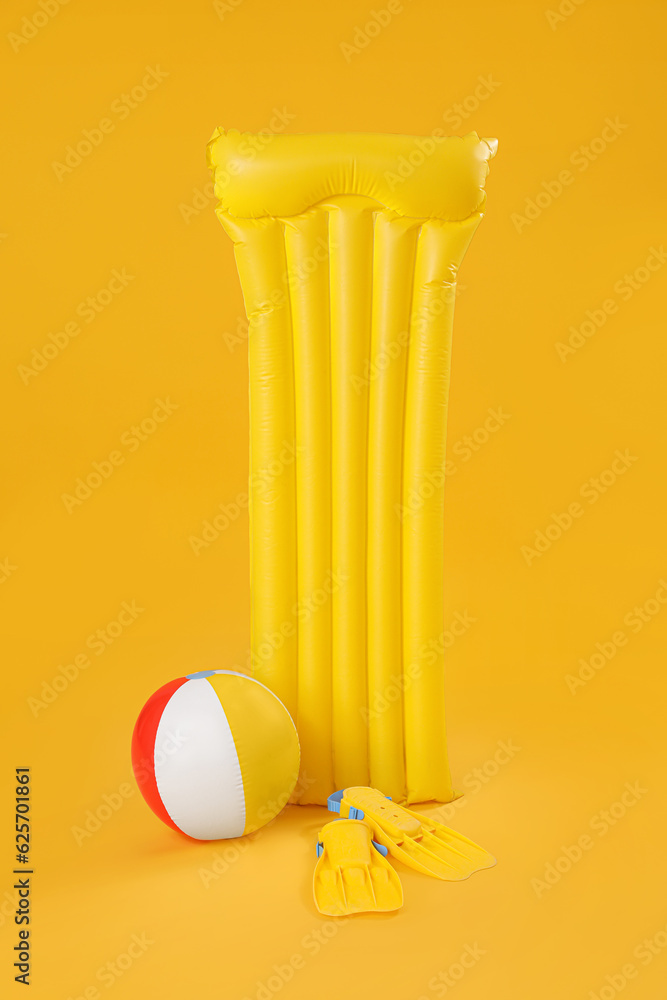 Inflatable mattress with beach ball and flippers on yellow background